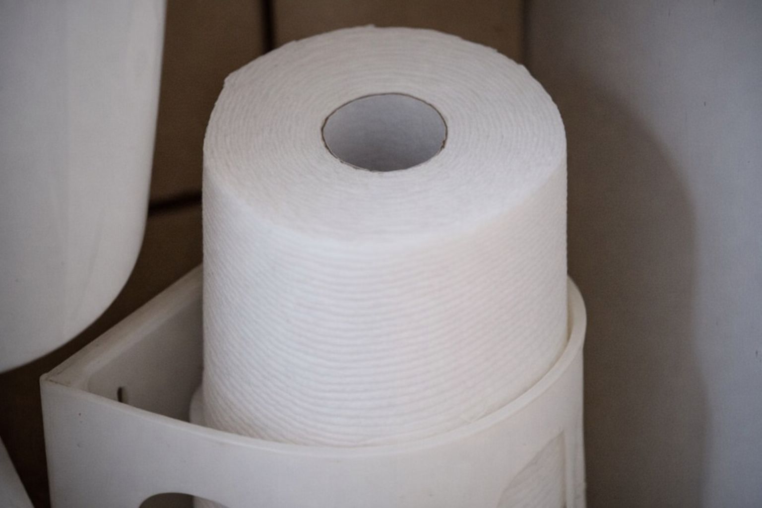 En hvit toalettrullholder i plast montert i et hjørne med en dorull.