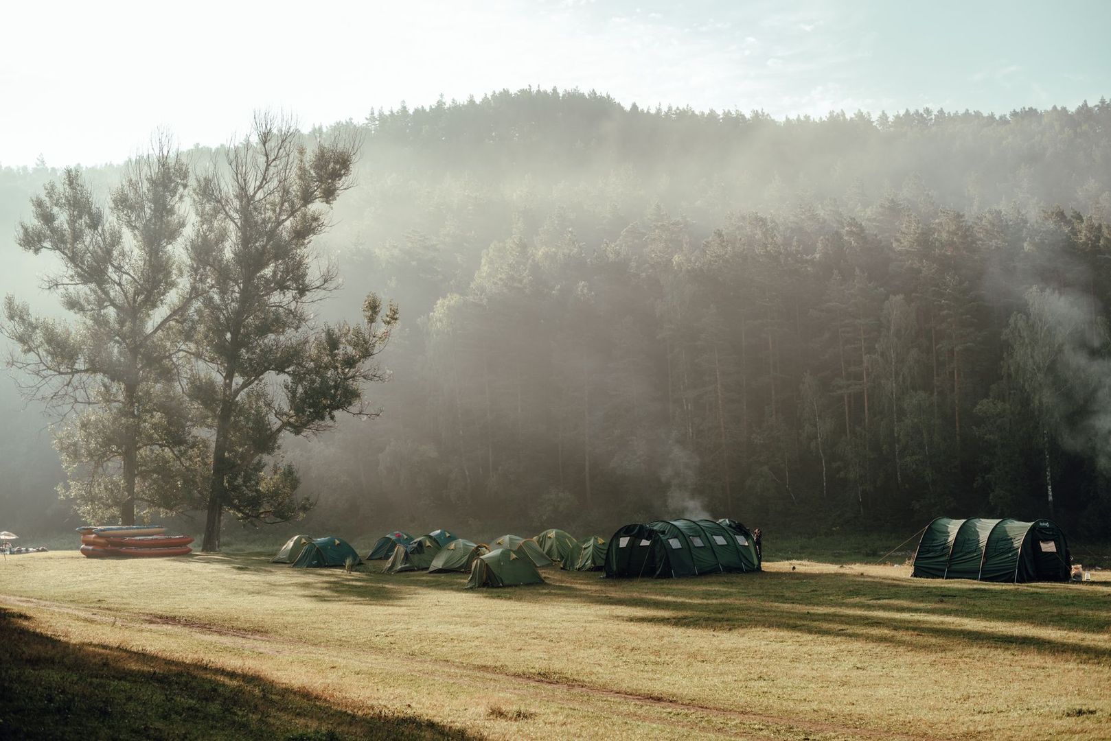 En teltleir på en gress slette omkranset av tåkete skog om morgenen.