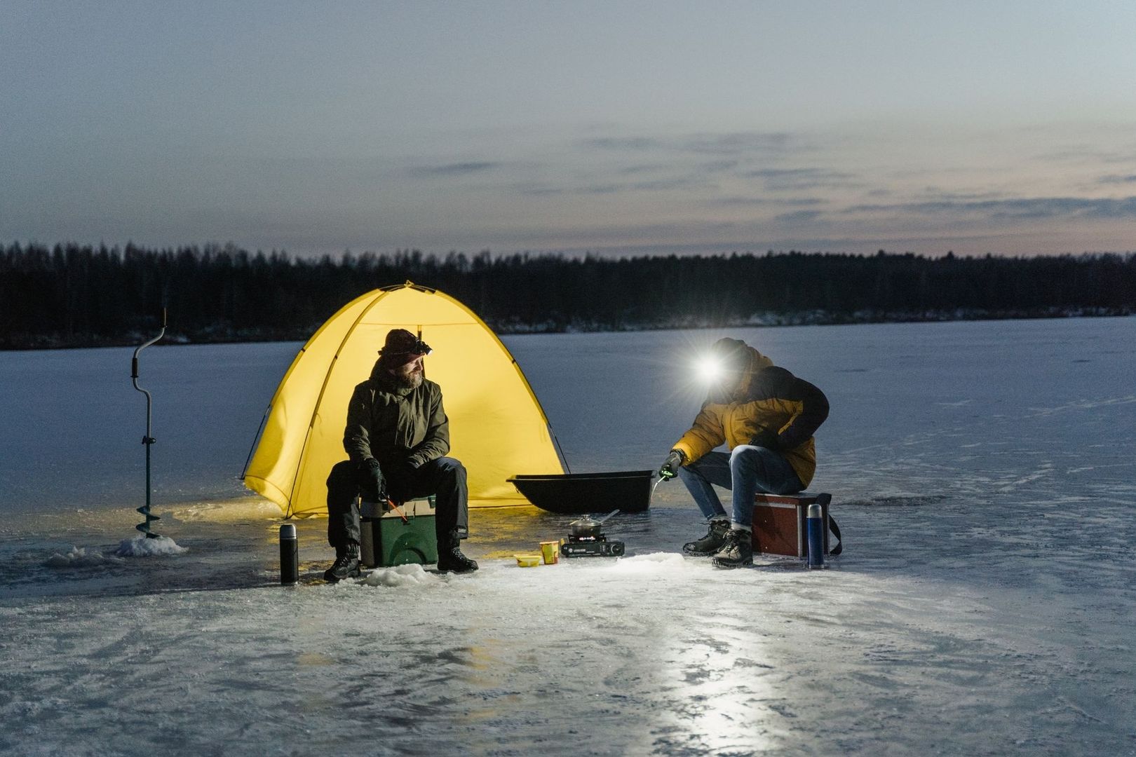 Vintercamping med multifuelbrenner, telt og isbor på en frossen innsjø
