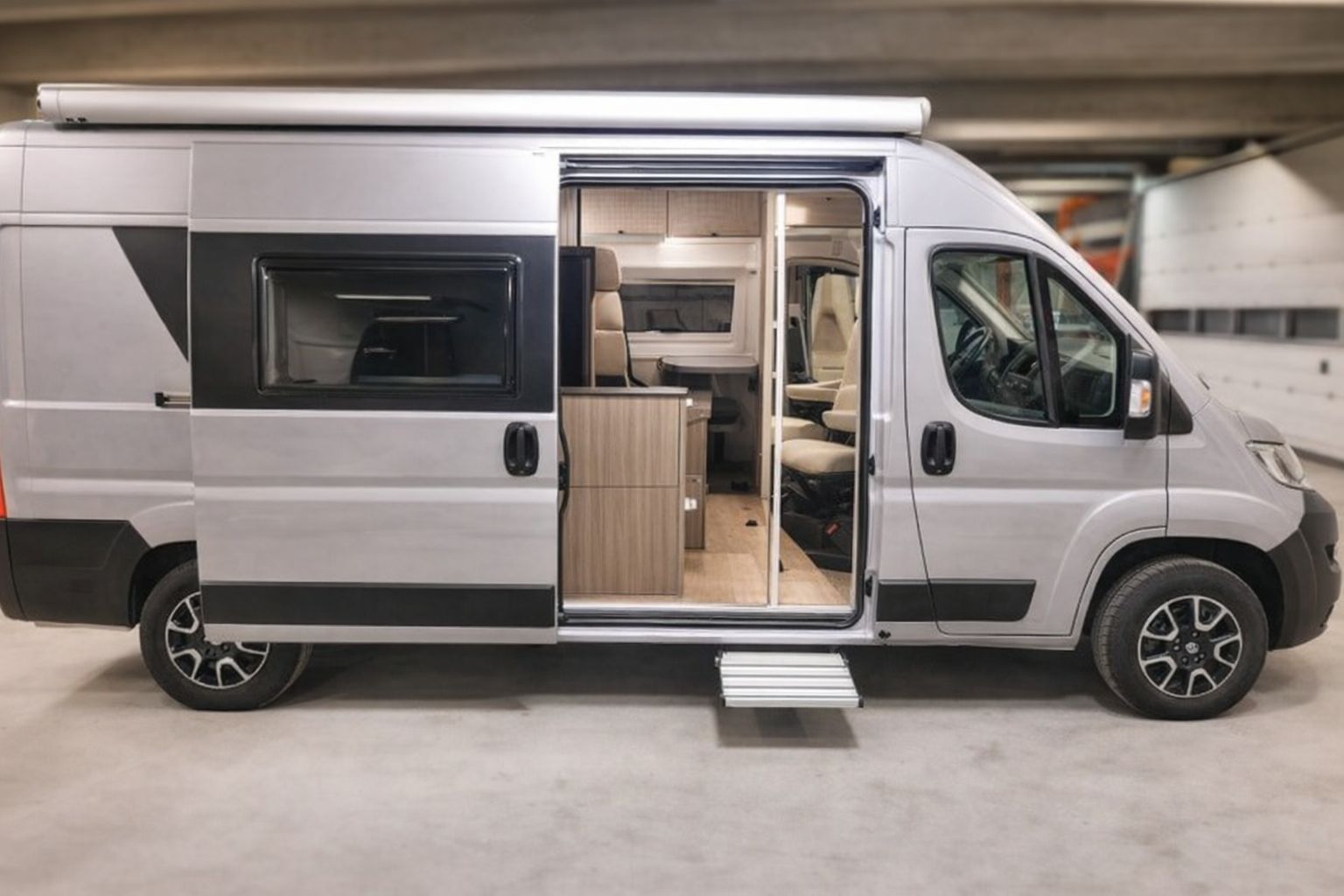 Sølvfarget bobil med åpen skyvedør som viser interiøret.
